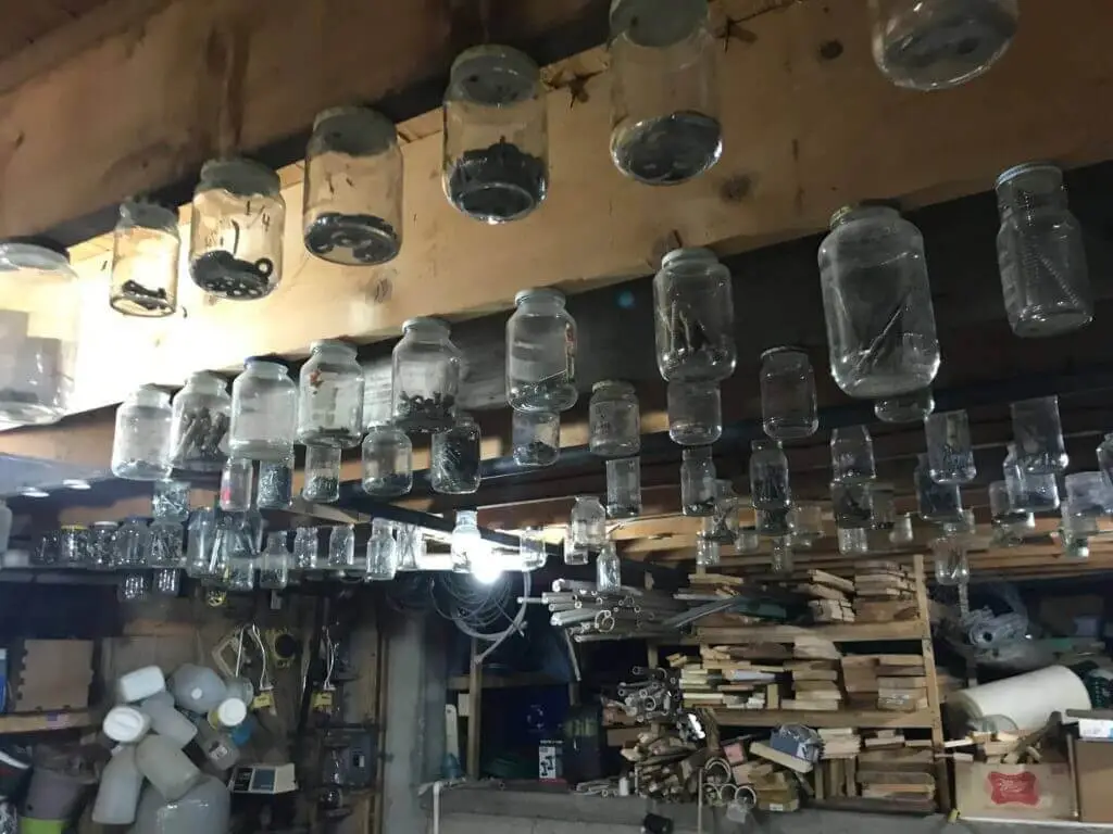 Glass jars hanging from the ceiling storing nuts, bolts, screws, and other parts.