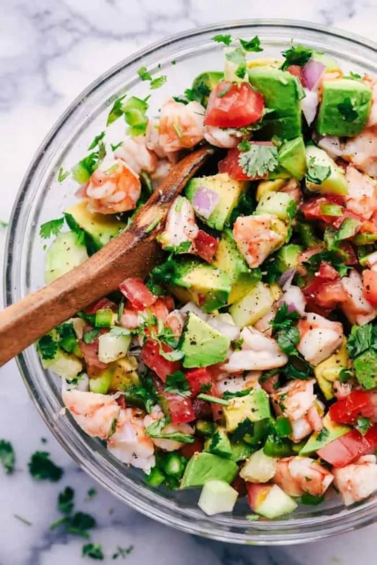 A colorful bowl of avocado shrimp cevice with a wooden spoon in it.