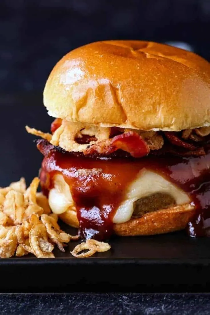 A large BBQ bacon turkey burger on a bun dripping with barbecue sauce, cheese, and fried onions.