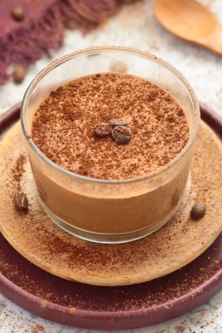 A cup of yummy coffee mousse topped with cocoa powder and coffee beans.