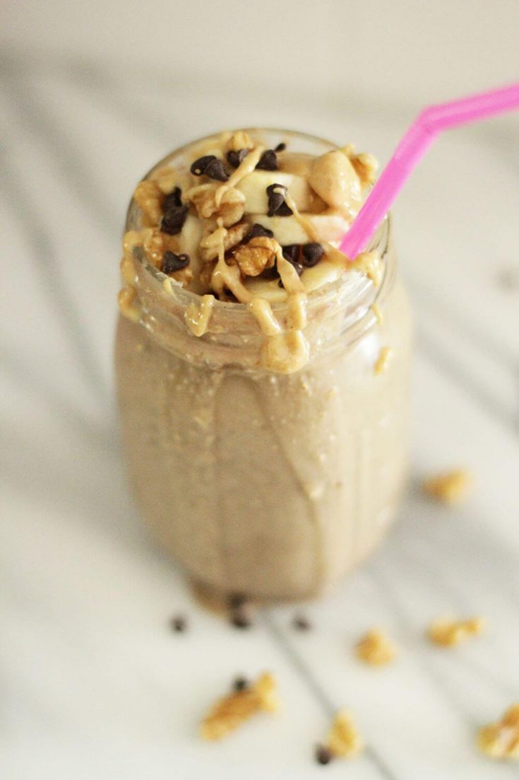 A delicious glass of caffeinated chocolate banana smoothie topped with peanut butter and chocolate chips.