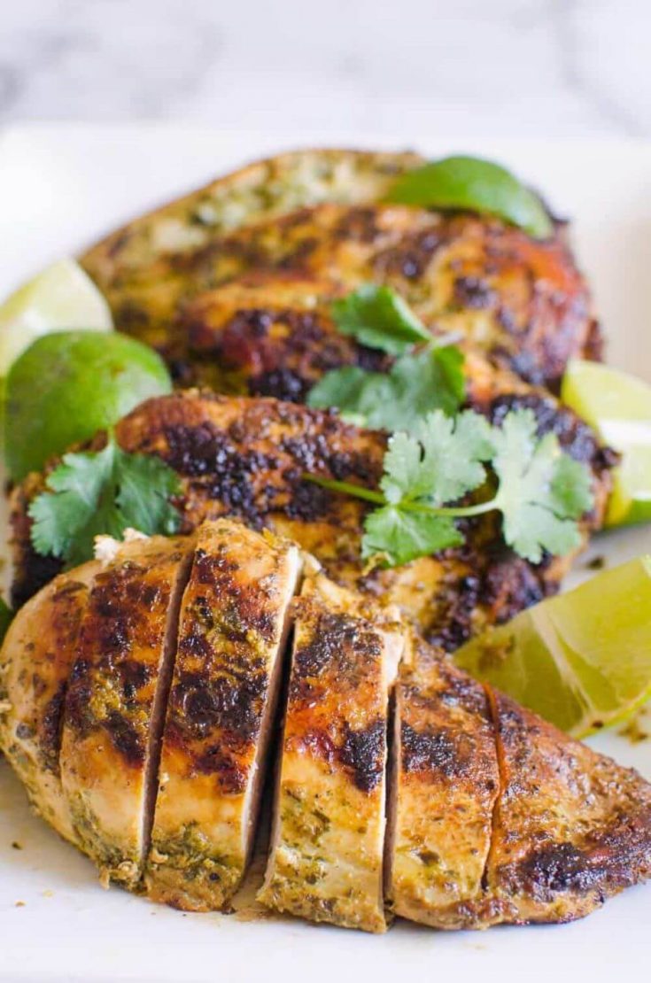 A plate of grilled cilantro lime chicken breasts topped with herbs.