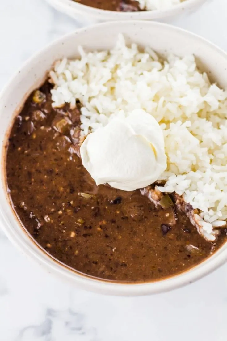 A large bowl of crock pot black bean soup with rice and a dollop of sour cream.