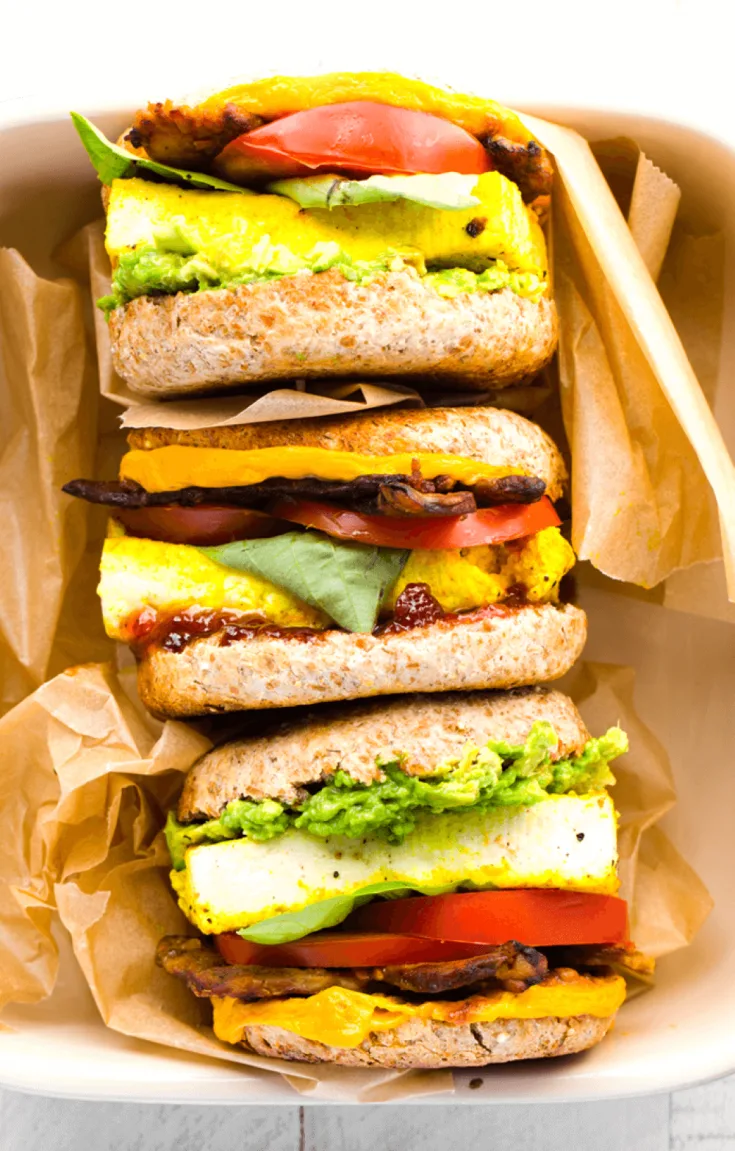 A stack of delicious vegan breakfast sandwiches with eggy tofu wrapped in brown paper.