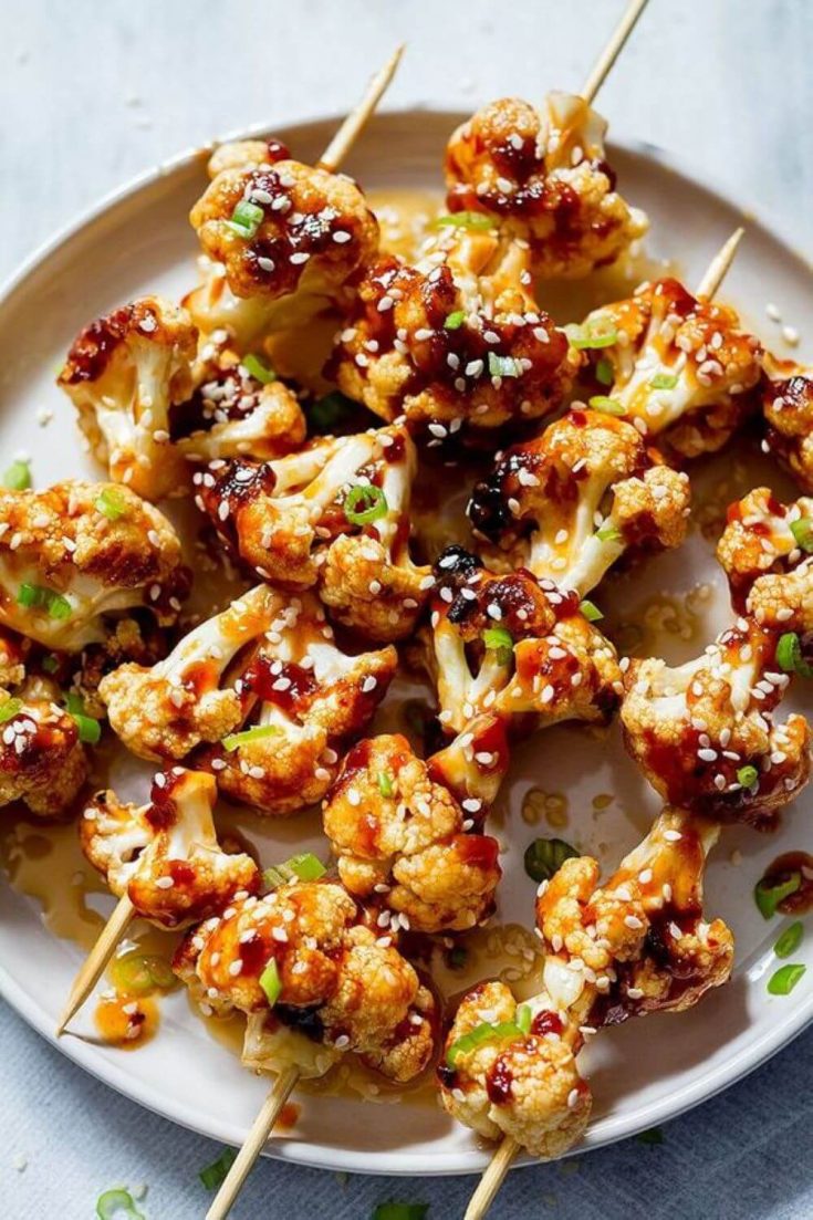 A large plate of saucy general tso's grilled cauliflower kabobs.