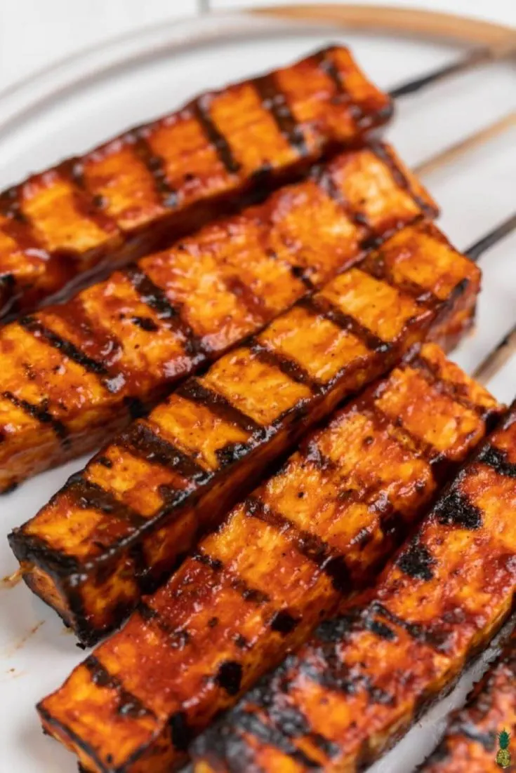 A closeup of several grilled barbecue tofu skewers.