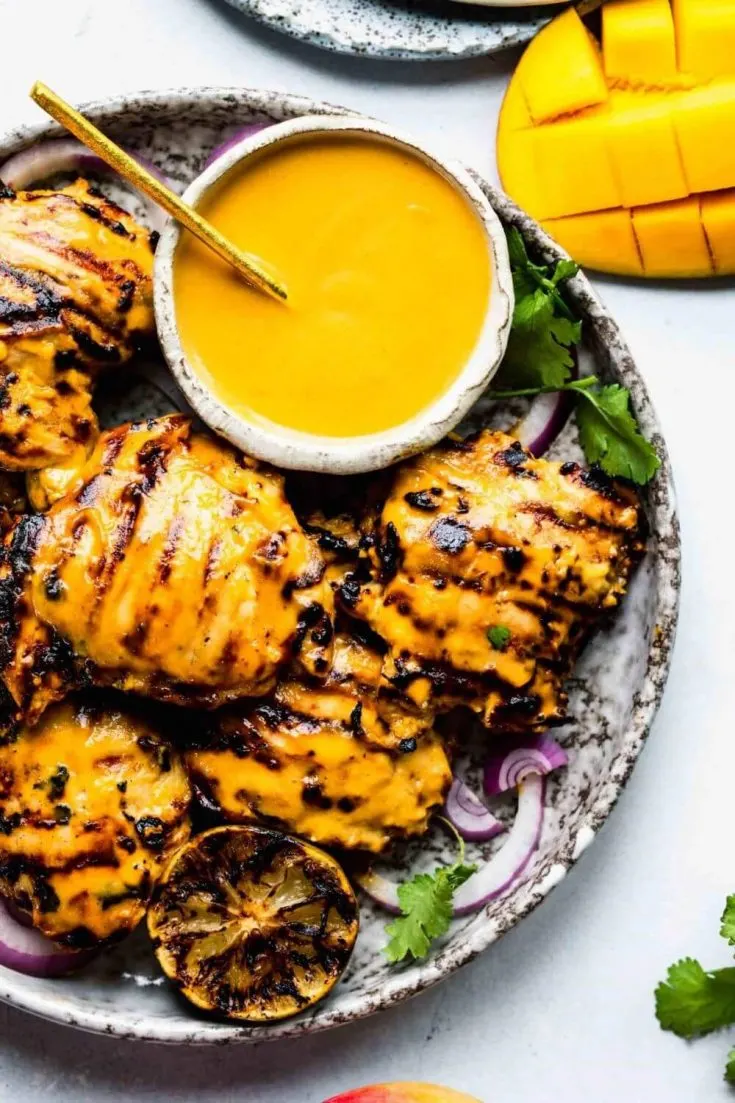 A plate of mango lime grilled chicken with a side of sauce.