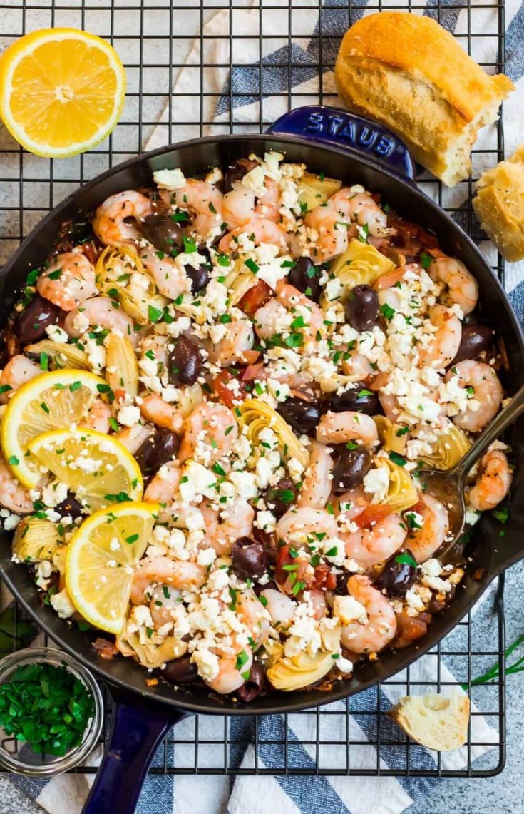 A full skillet of Mediterranean shrimp topped with feta cheese and lemon slices.