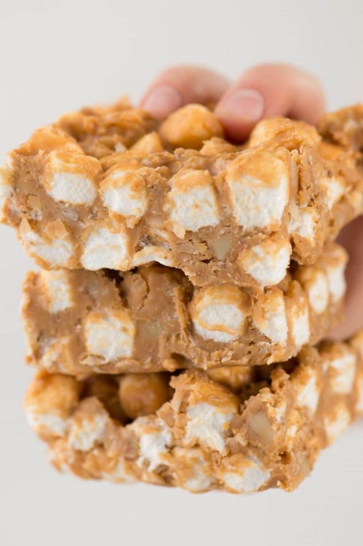 A hand holding a stack of three no-bake butterscotch marshmallow bars.