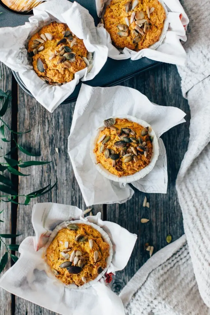 Several healthy savory carrot and zucchini muffins topped with nuts and seeds.