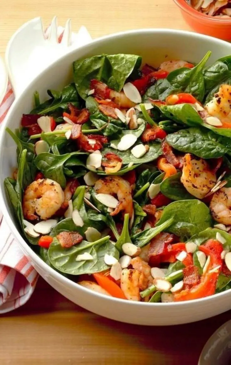A healthy bowl of shrimp and spinach salad topped with hot bacon dressing.