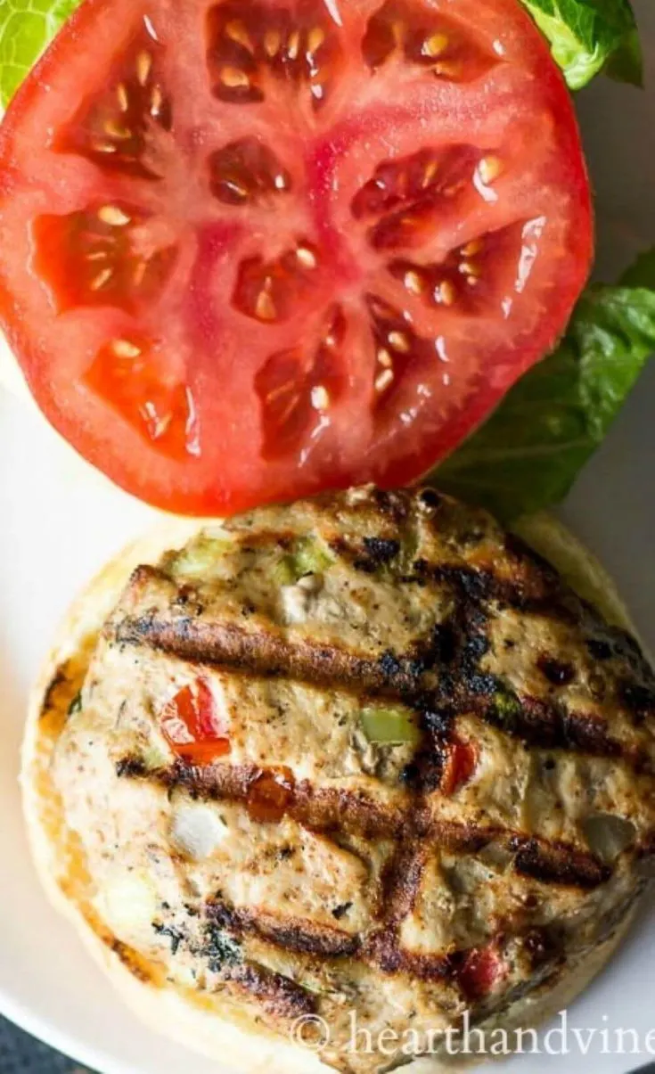 An open-faced Southwest turkey burger with tomato and lettuce near by.