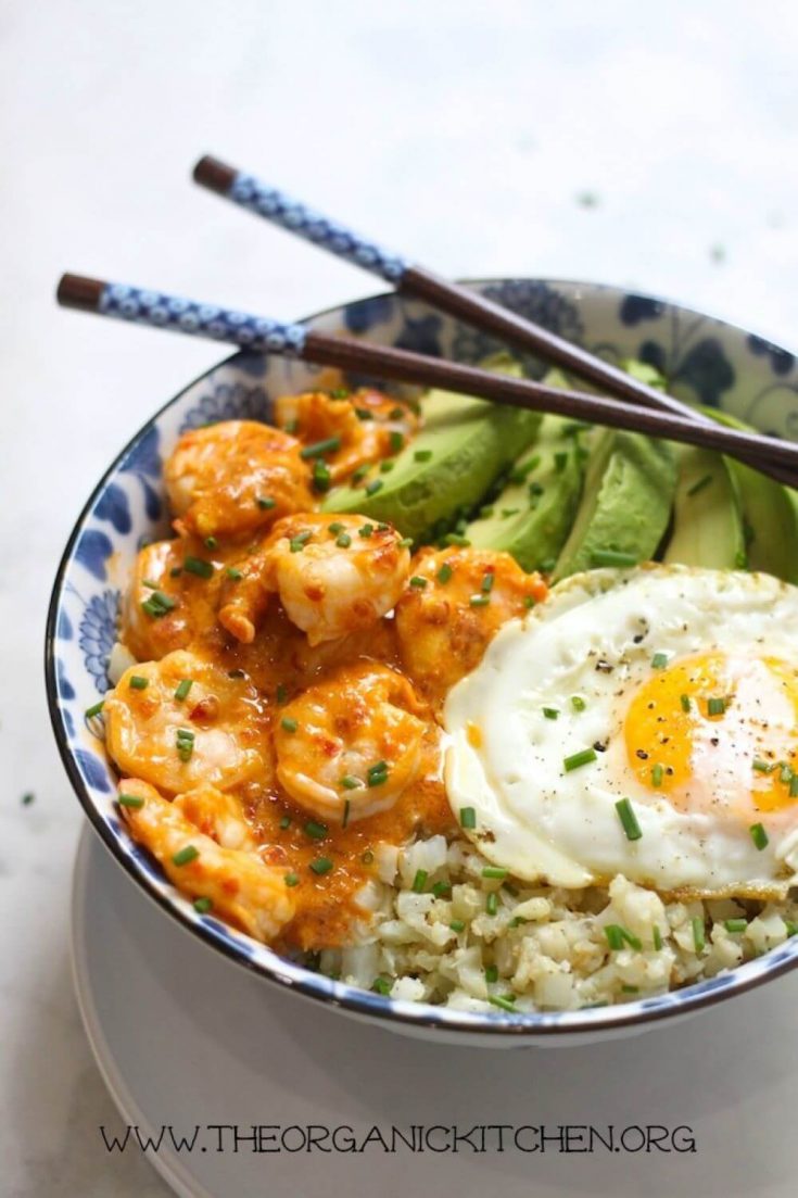 A bowl full of spicy shrimp and cauliflower rice bowl topped with an egg and avocado.