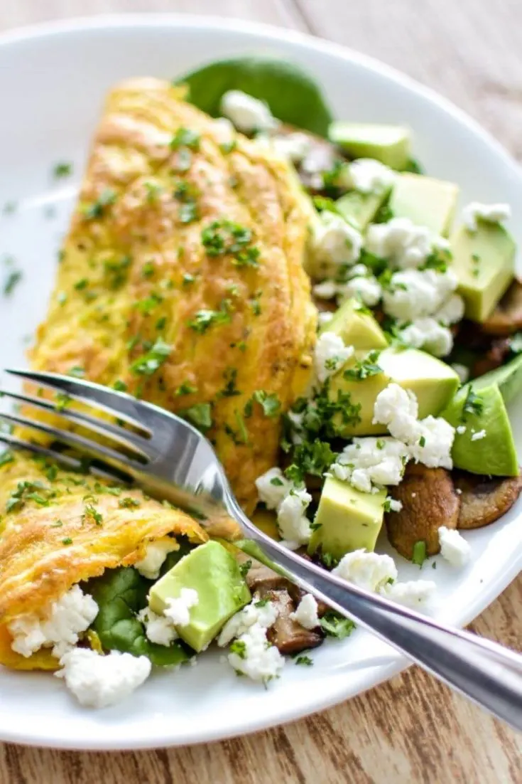 A stuffed spinach avocado goat cheese omelette with a fork cutting through it.