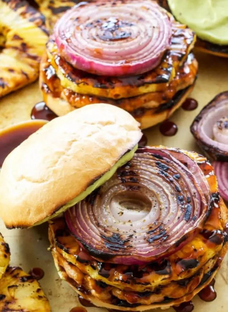 Two teriyaki turkey burgers on buns topped with grilled pineapple and onions.
