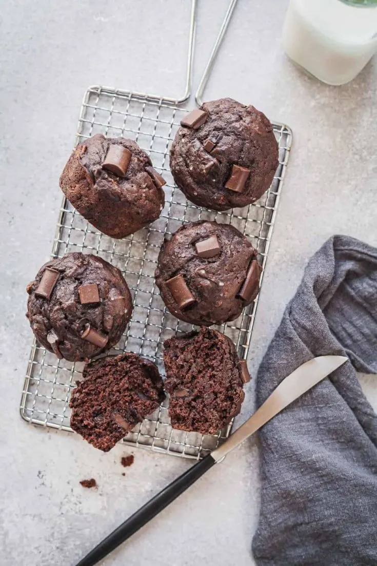 Several delicious vegan chocolate zucchini muffins set out on a cooling rack.