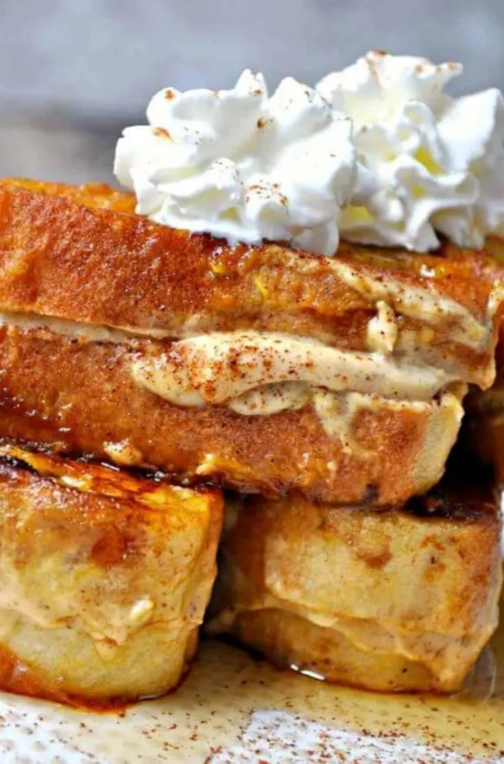 A close-up of a stack of vegan pumpkin cheesecake stuffed french toast topped with whipped cream.