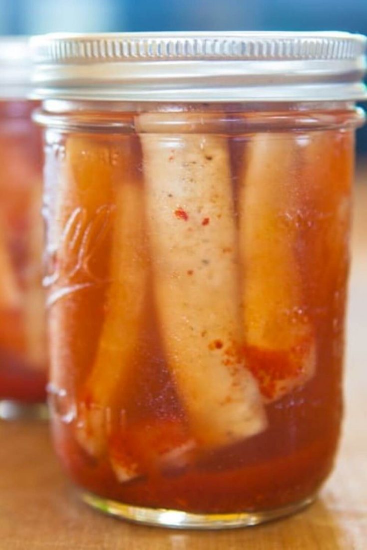 A closeup mason jar full of fermented spicy daikon radish spears.