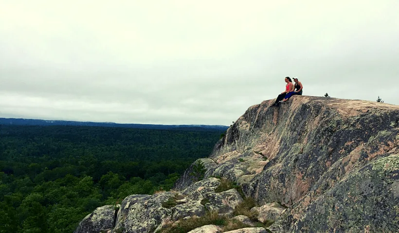 Two women sitting atop of a huge rock ledge on top of Hogback Mountain in Marquette, Mi.
