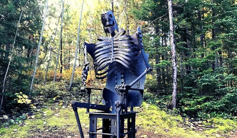 A sculpture of a skeleton sitting in a chair made out of scrap iron and metals.