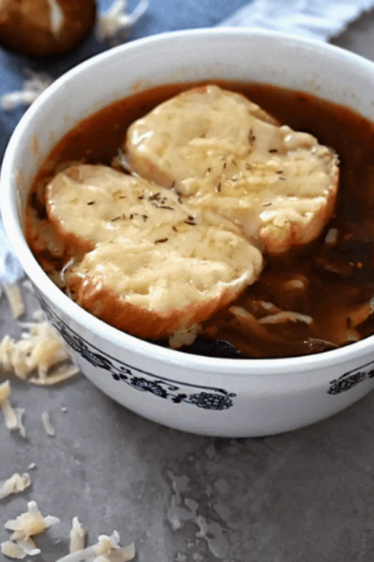 A closeup bowl of vegetarian french onion soup topped with cheese and crostinis.