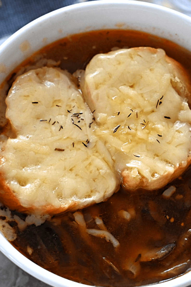 A closeup view of a bowl of vegetarian French onion soup topped with toasted baguettes and Gruyere cheese.