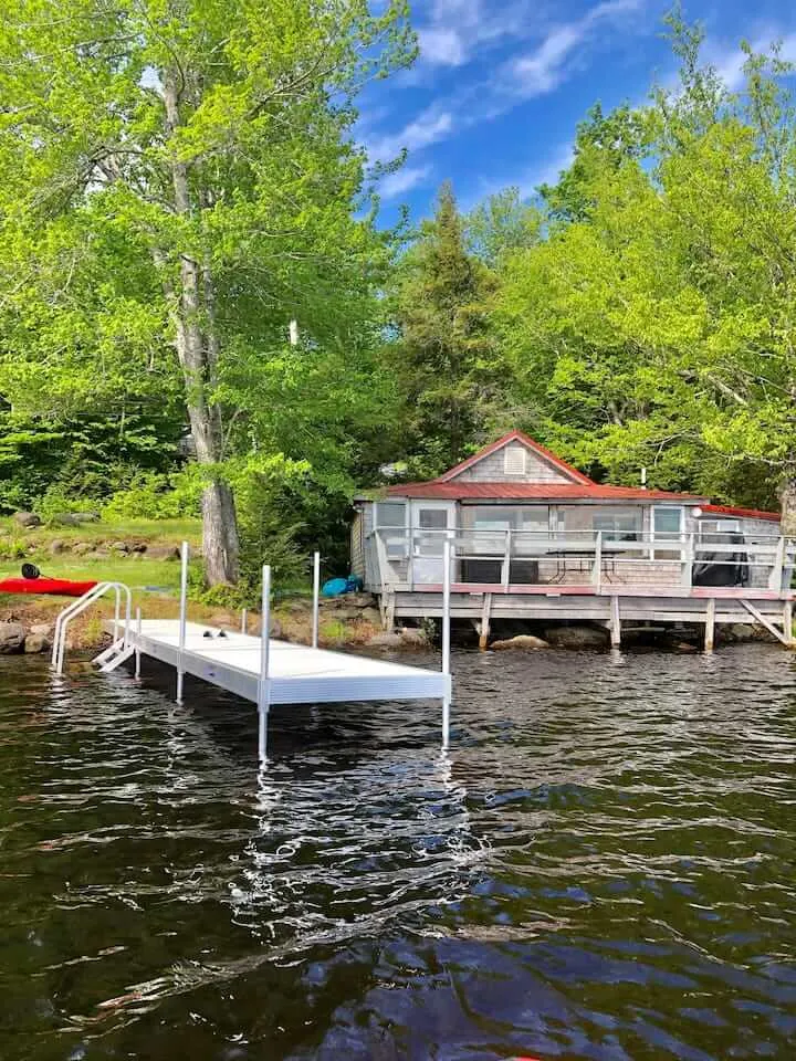A small cabin on a lake in Maine next to a dock.