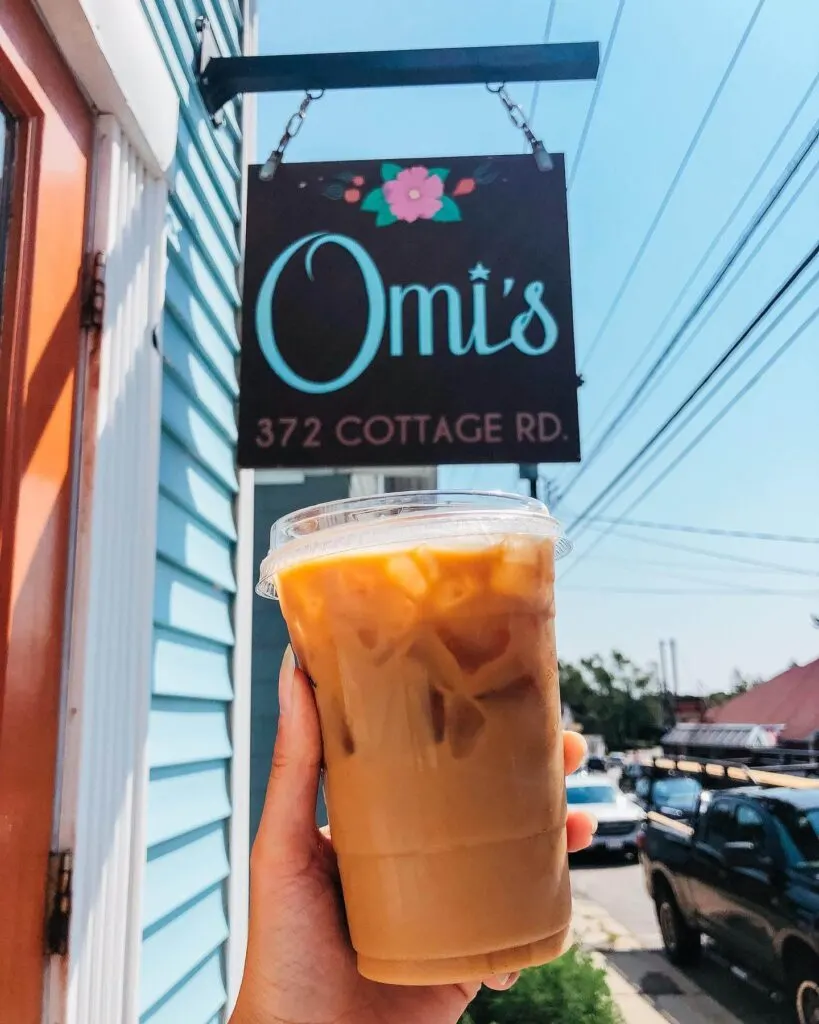 A cup of iced coffee being held up to the Omi's Coffee Shop sign in South Portland.