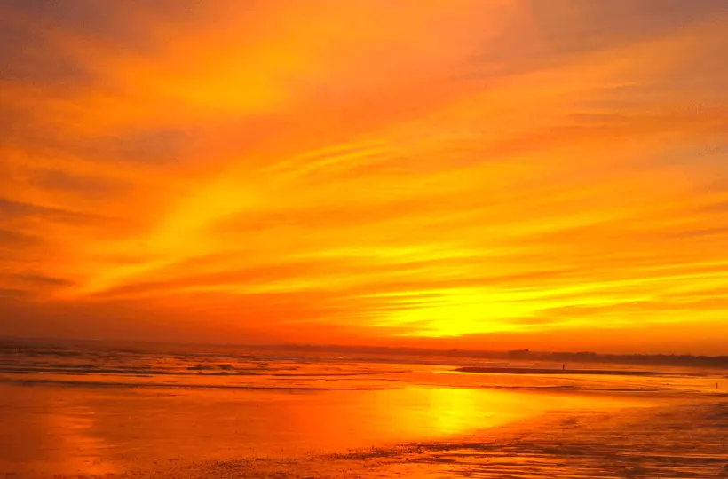 A sunset glowing orange and red over the Atlantic Ocean on a beach.