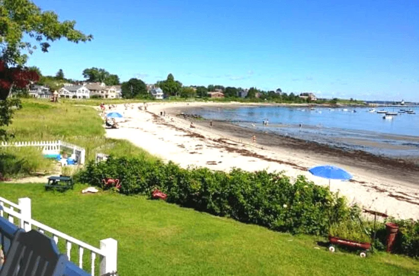 A white sand beach near the ocean with grass and houses in the background.