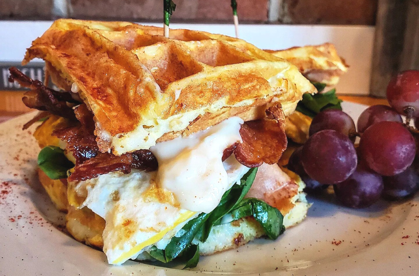 A large breakfast sandwich with egg, spinach, and bacon on a waffle.
